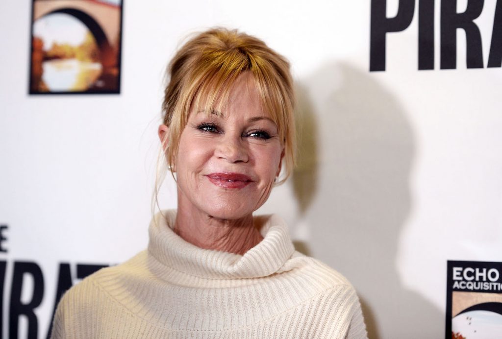 Un gros plan de Melanie Griffith dans un pull à col roulé blanc et ses cheveux relevés.