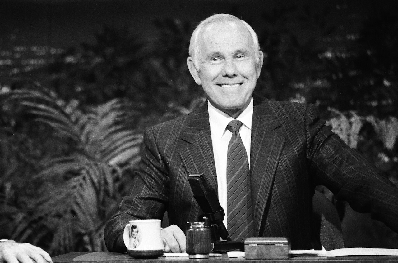 Photo en noir et blanc de Johnny Carson en costume derrière le bureau de 