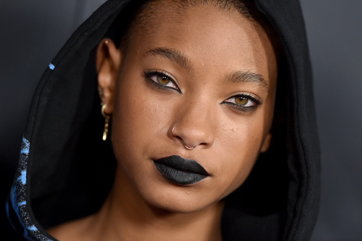 Willow Smith porte du rouge à lèvres noir et une capuche sur la tête.