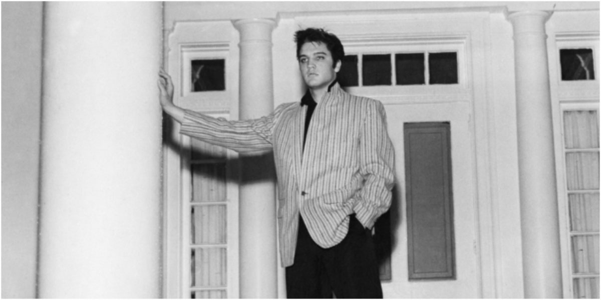Elvis Presley pose devant Graceland dans une image en noir et blanc.