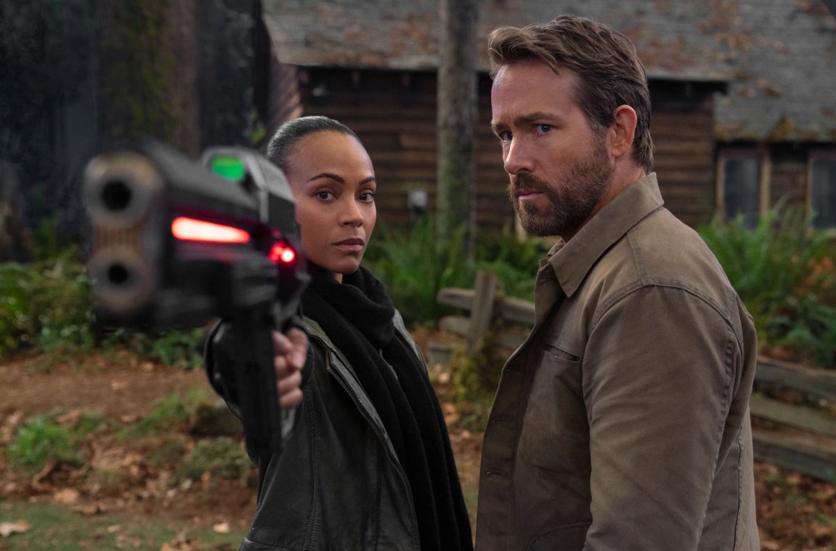 'The Adam Project' Zoe Saldana dans le rôle de Laura et Ryan Reynolds dans le rôle de Big Adam pointent une arme vers la caméra
