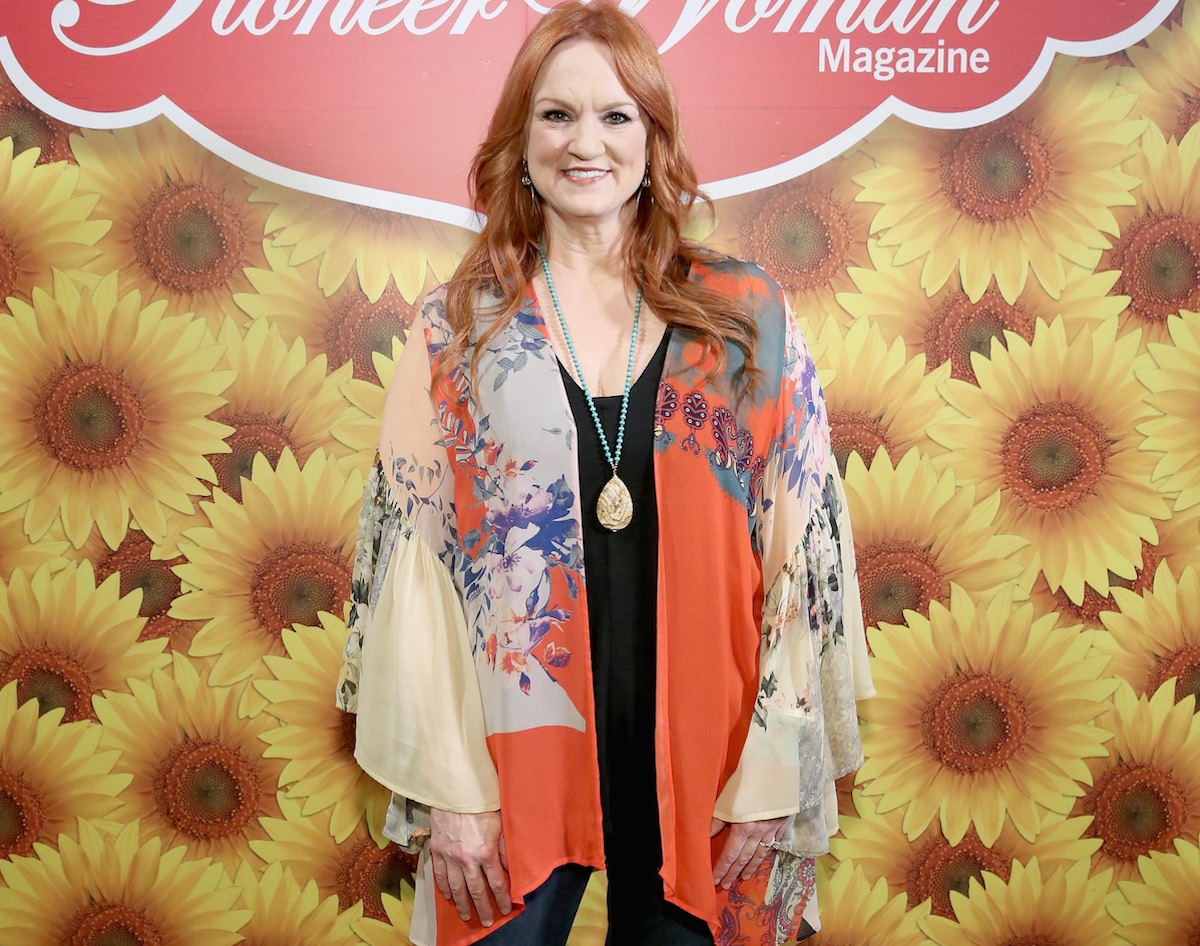 Ree Drummond sourit debout devant une pancarte Pioneer Woman