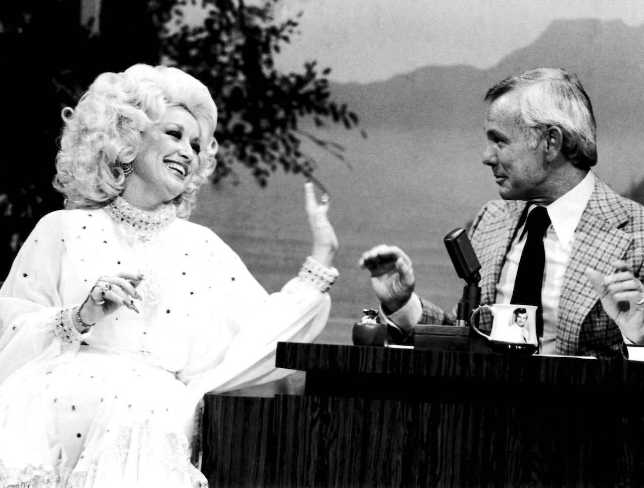 Photo en noir et blanc de Dolly Parton riant et tendant la main vers Johnny Carson dans 