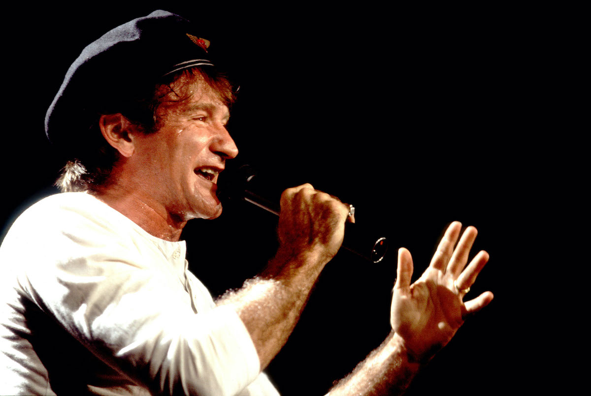 Robin Williams porte un chapeau et parle dans un microphone