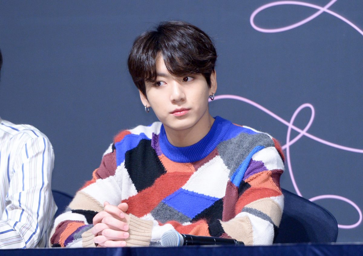 Jungkook, membre du BTS, portant une chemise colorée et serrant sa main sur une table