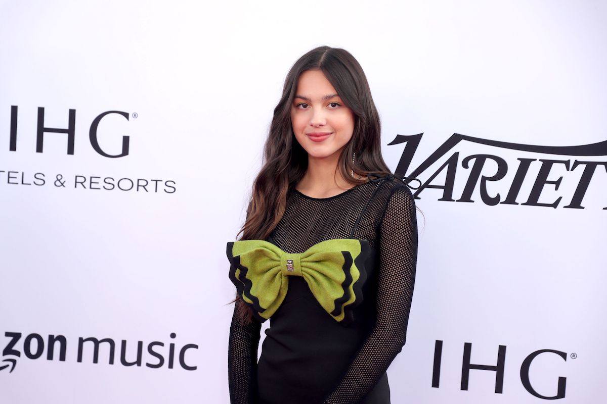 Olivia Rodrigo pose dans une robe noire avec un gros nœud vert lors d'un événement.