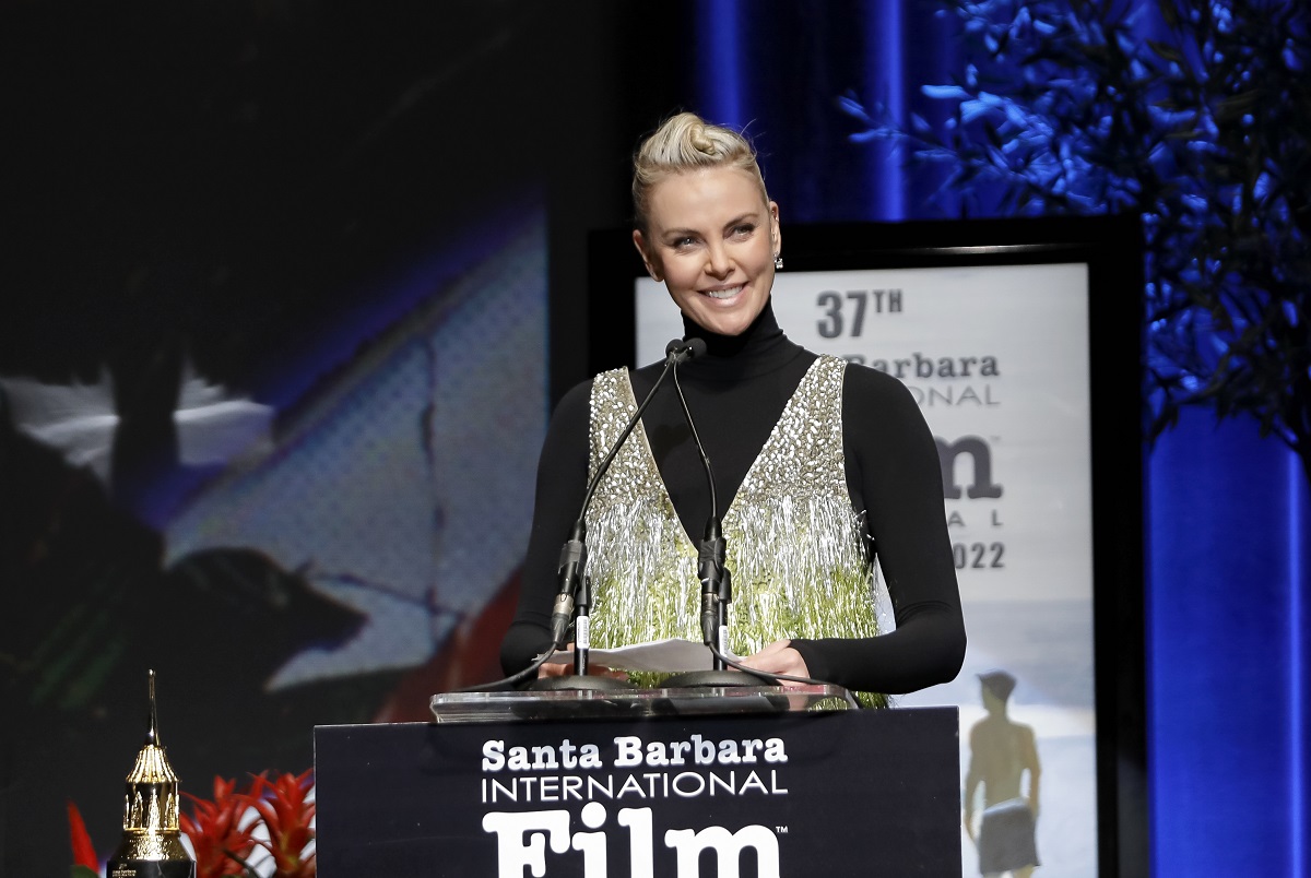 Charlize Theron s'exprimant sur scène tout en portant une robe noire et dorée.