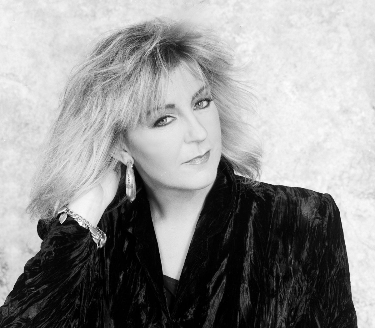 Une photo en noir et blanc de Christine McVie portant une veste en velours et des créoles. 
