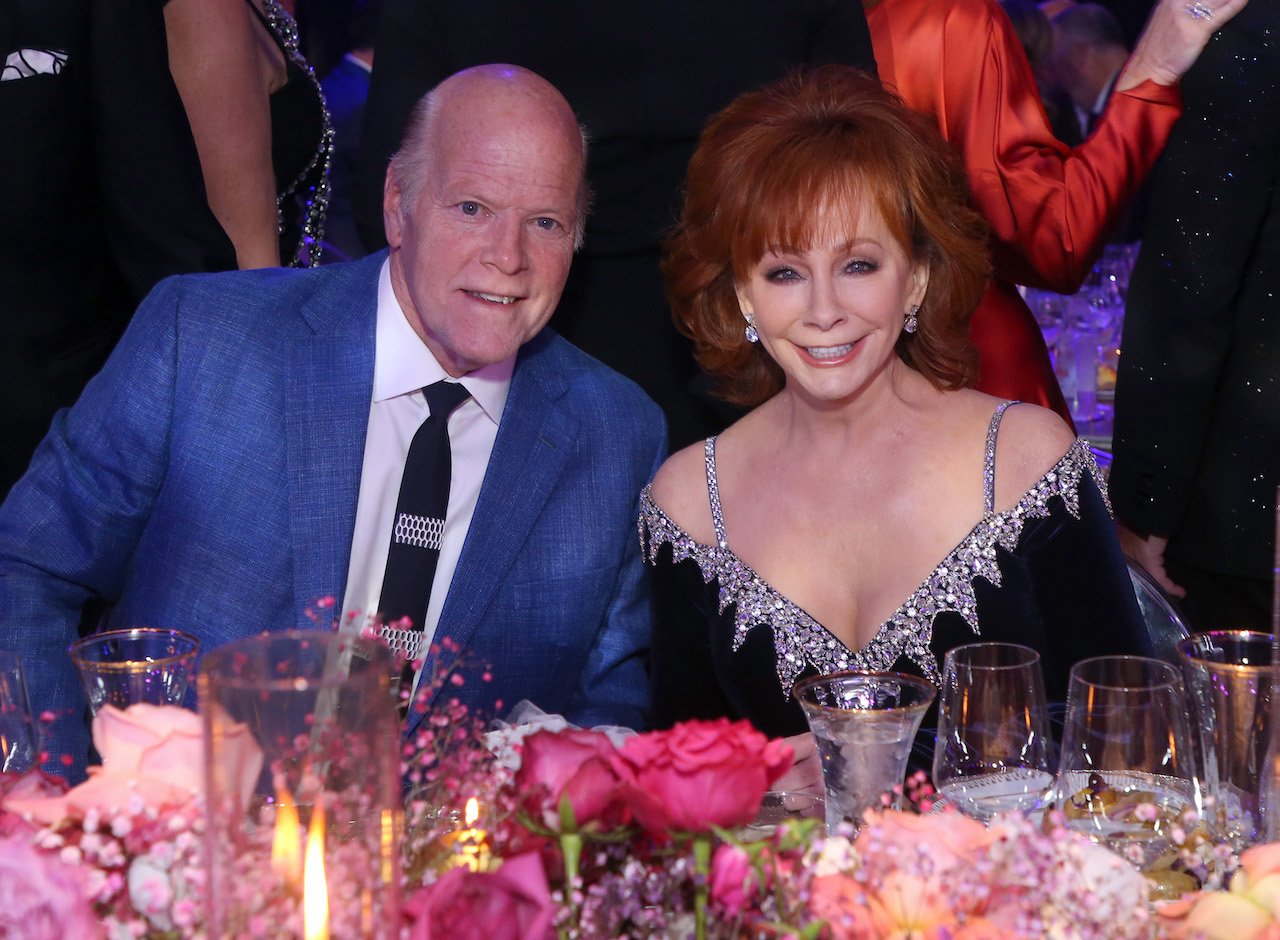 (LR) Rex Linn dans une veste bleue et Reba McEntire dans une robe bleu foncé, assis à une table et souriant