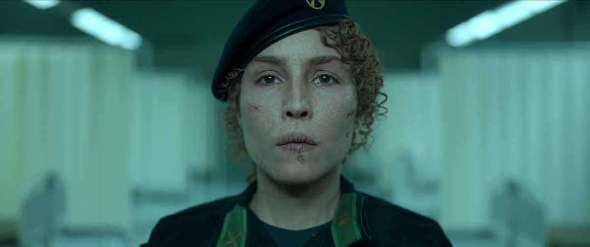 'Black Crab' Noomi Rapace dans le rôle de Caroline Edh regardant droit devant avec des lèvres craquelées et un chapeau militaire