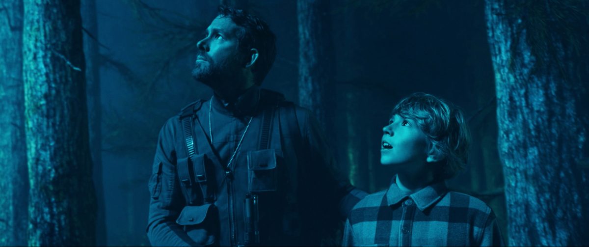 'The Adam Project' Ryan Reynolds comme Big Adam et Walker Scobell comme Young Adam regardant la lumière bleue dans la forêt