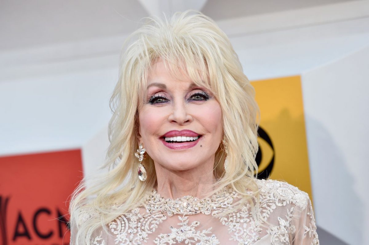 Dolly Parton porte une robe en dentelle blanche et des boucles d'oreilles en cristal. 