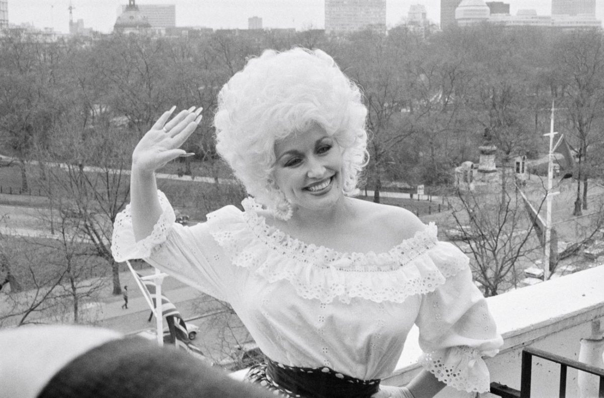 Une photo en noir et blanc de Dolly Parton debout sur un balcon et agitant la main.