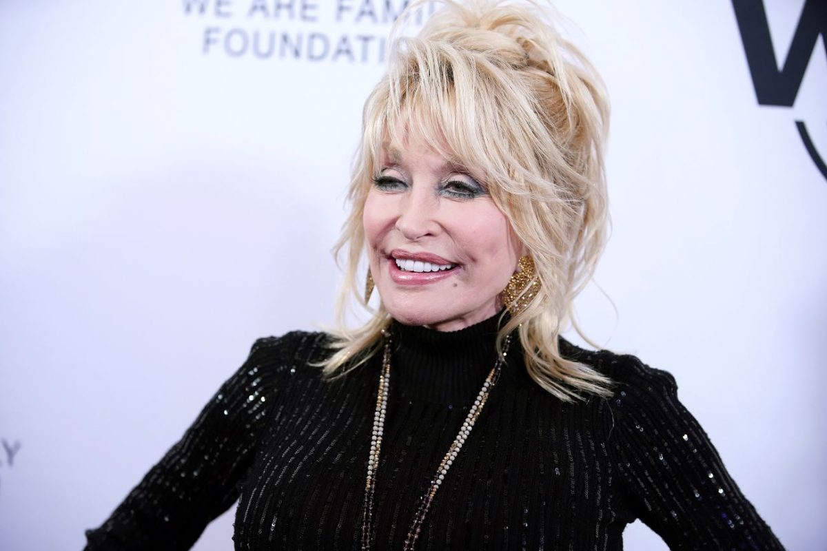 Dolly Parton porte une robe noire et se tient devant un fond blanc. Dolly Parton envisagerait de se jouer dans un film sur sa vie.