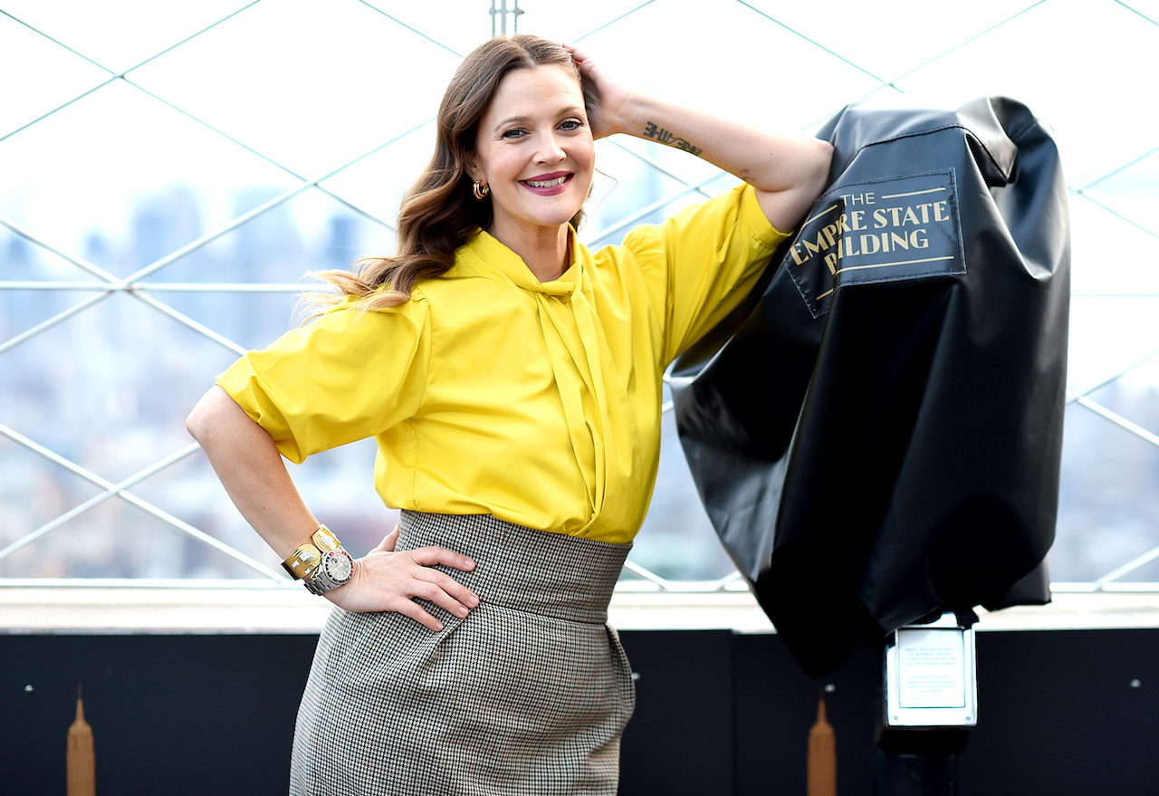 Drew Barrymore en haut jaune, souriant et appuyé sur un coude avec l'autre main sur sa hanche