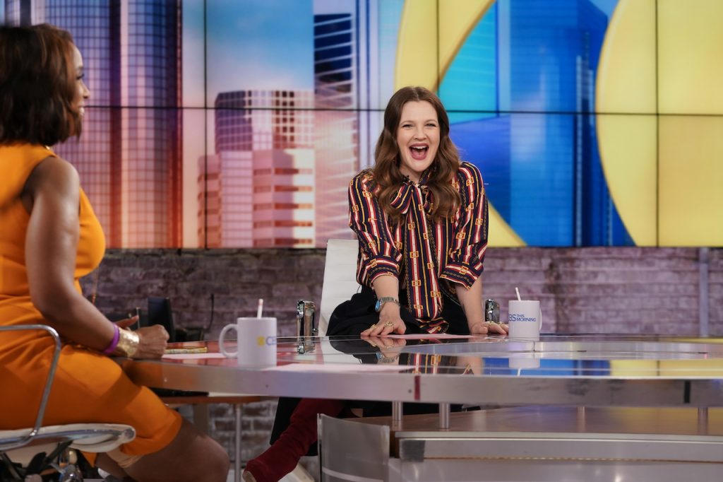 Drew Barrymore assis et vêtu d'une chemise rayée, souriant