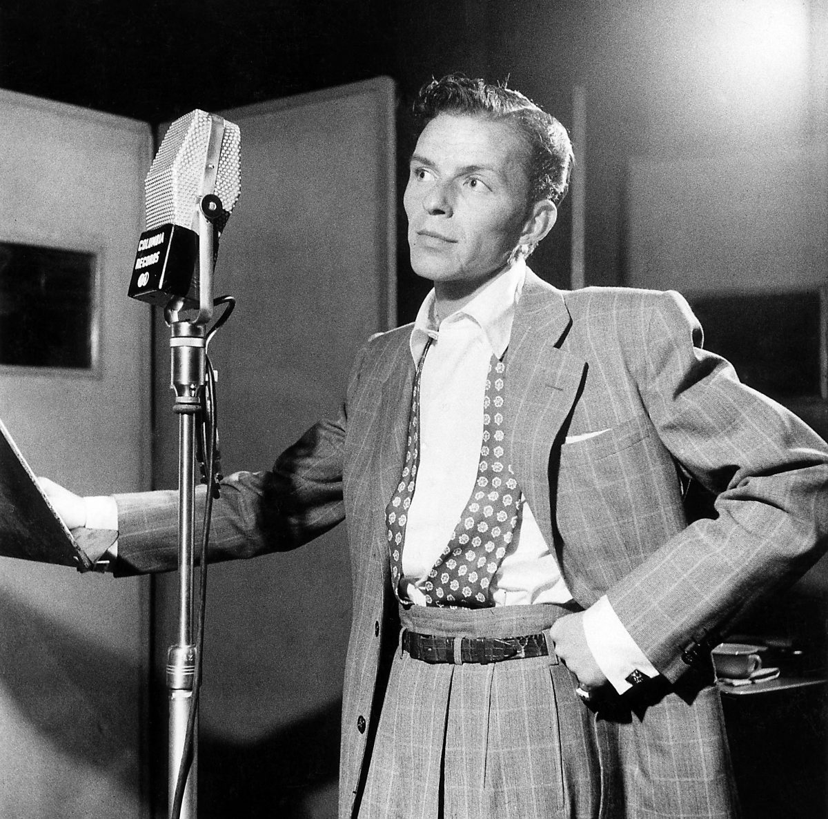 Frank Sinatra porte un costume et se tient devant un micro. 