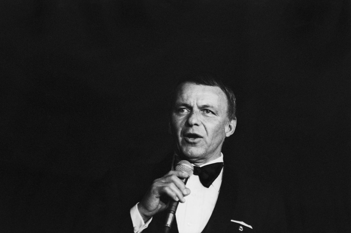 Une photo en noir et blanc de Frank Sinatra portant un smoking et tenant un microphone.