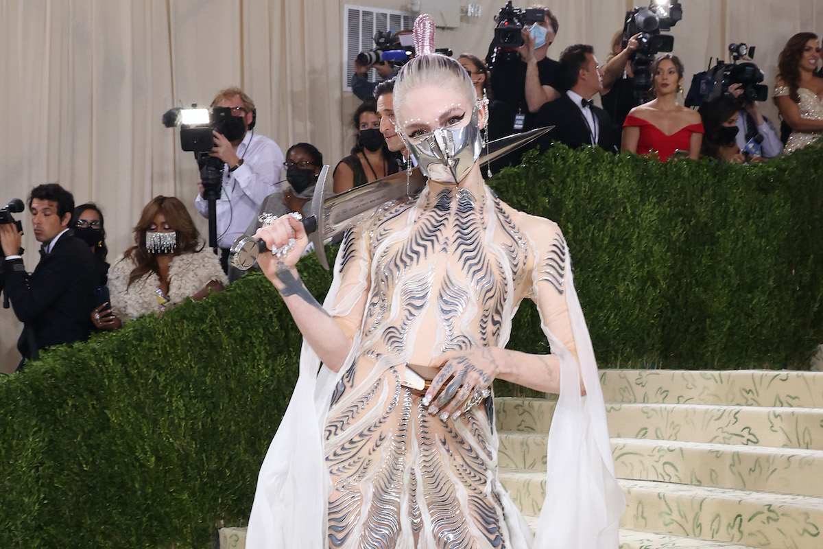 Grimes portant un masque argenté, tenant une épée