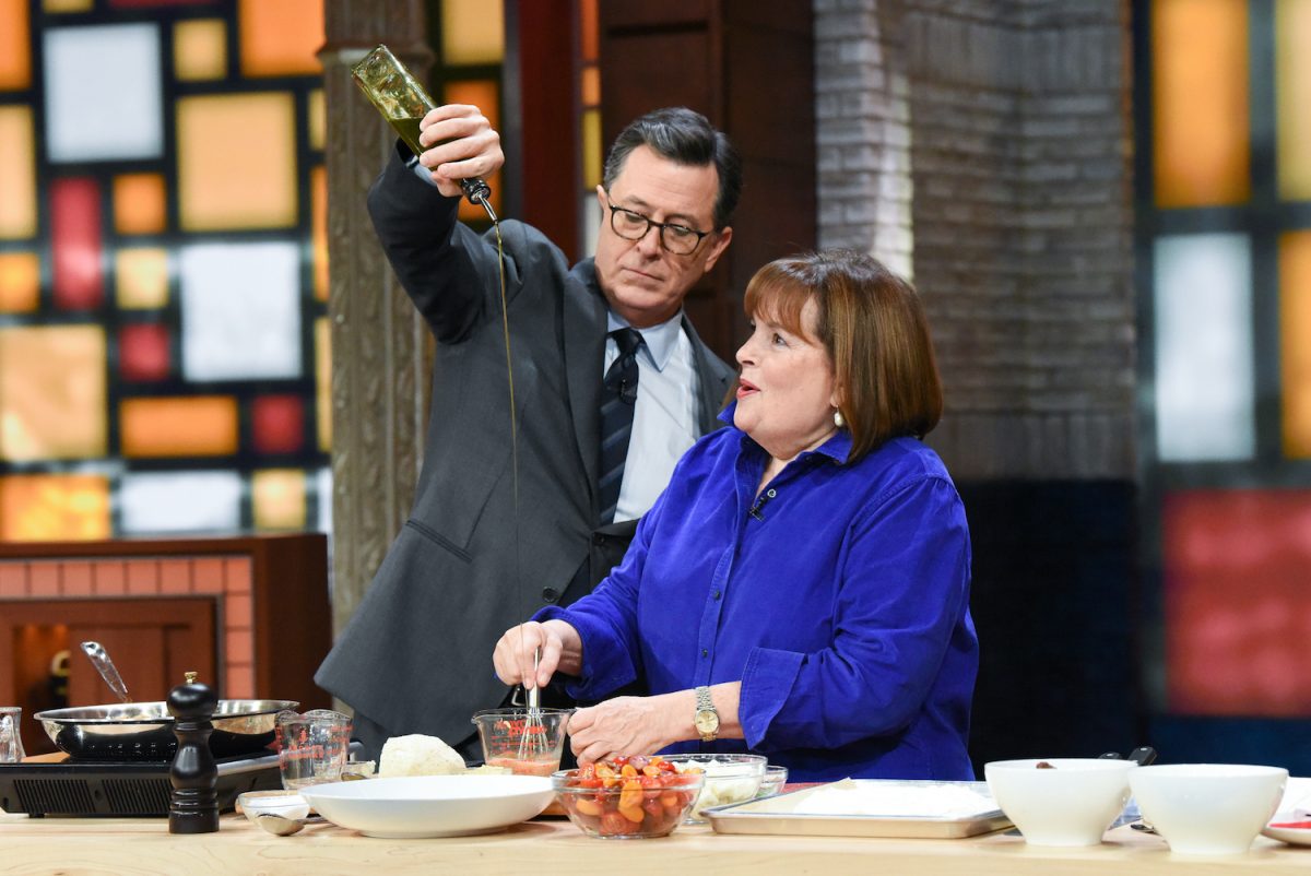 Ina Garten porte une chemise bleu vif et cuisine avec Stephen Colbert que l'on voit arroser d'huile