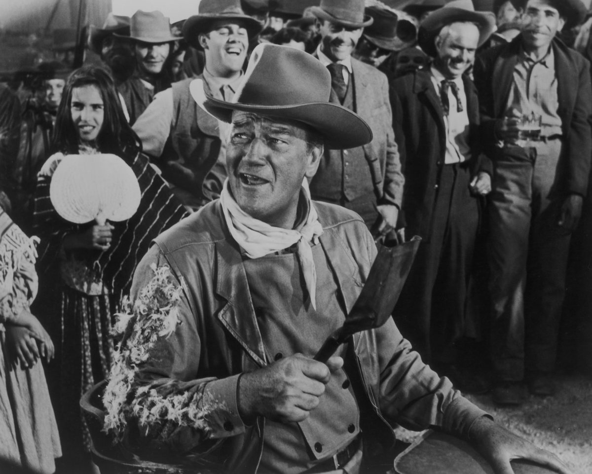 John Wayne comme George Washington 'GW' McLintock dans 'McLintock!' portant son costume, regardant sur le côté, debout devant un groupe de personnes