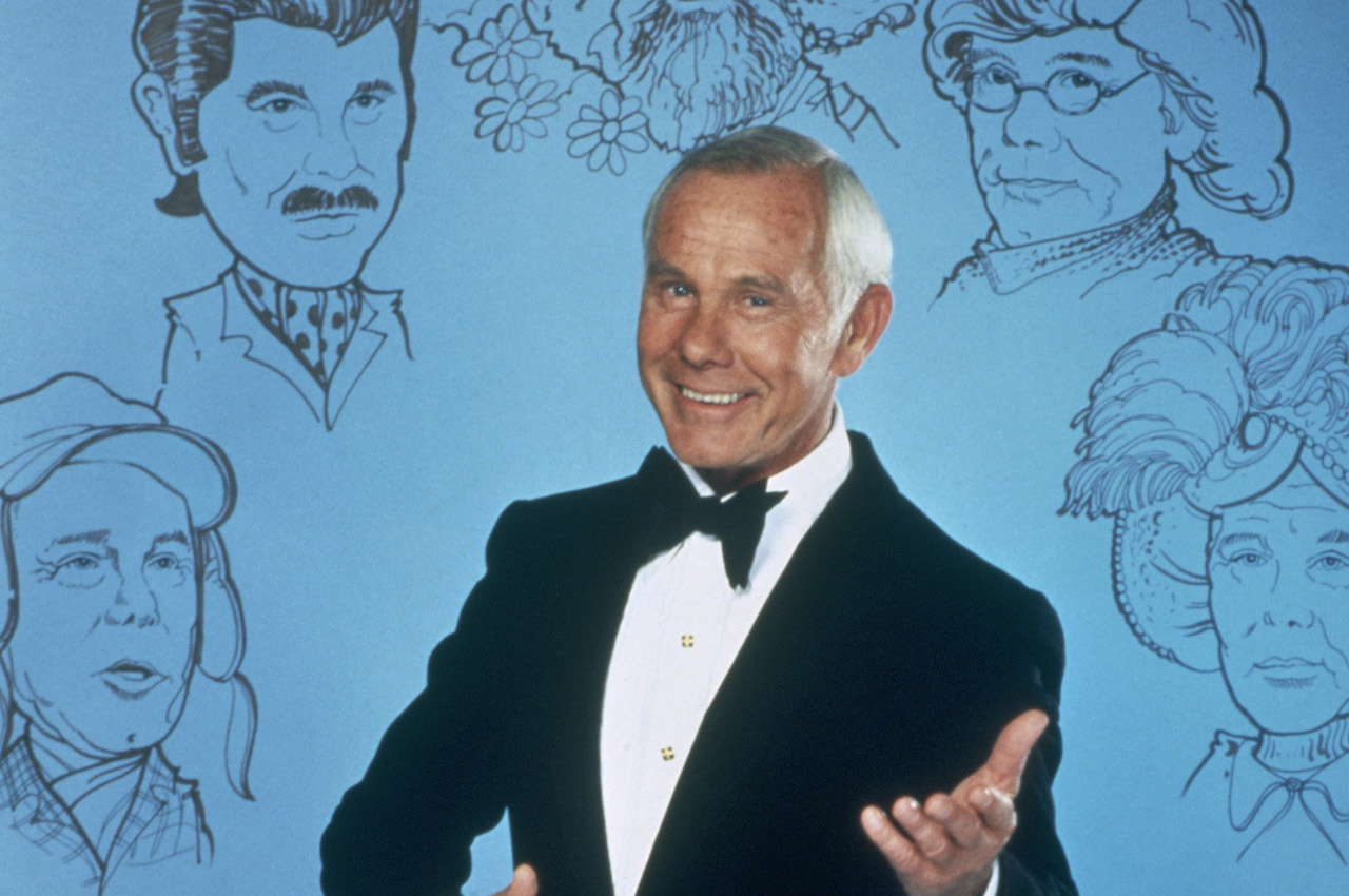 Johnny Carson se tient devant un fond bleu décoré de dessins de certains de ses célèbres personnages de croquis de 