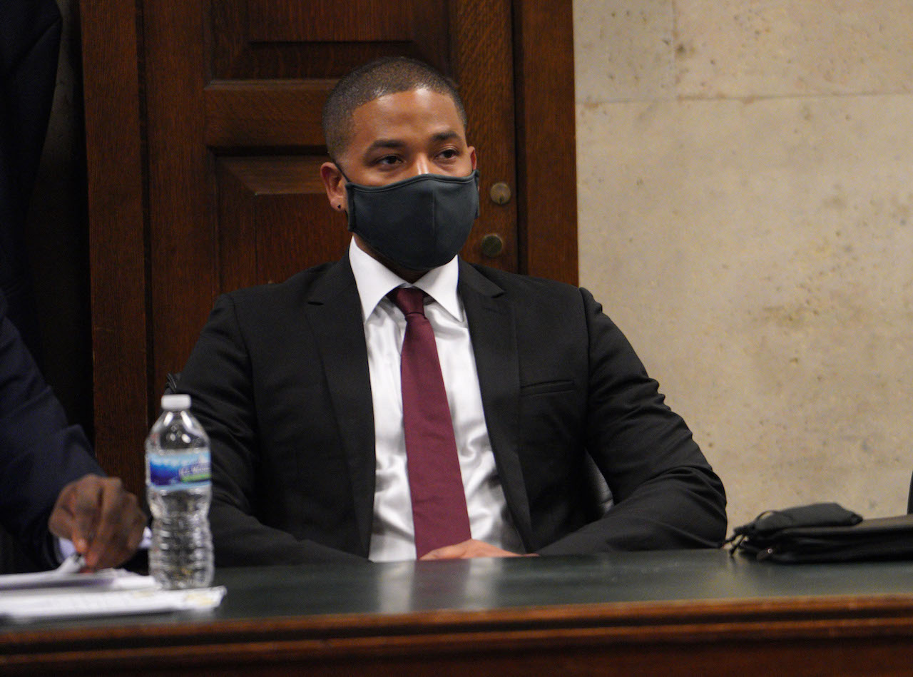 Jussie Smollett en costume-cravate portant un masque noir et assis à une table lors de sa condamnation
