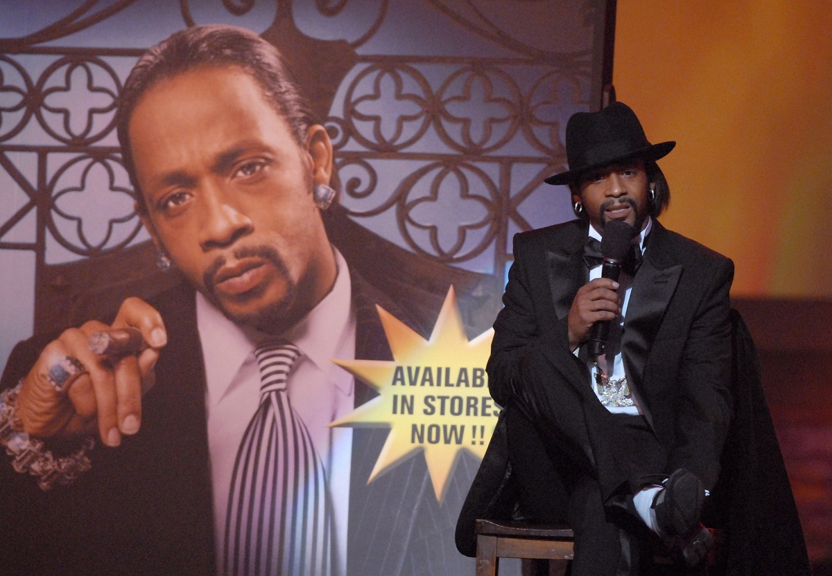 Katt Williams tenant un microphone tout en portant un costume.