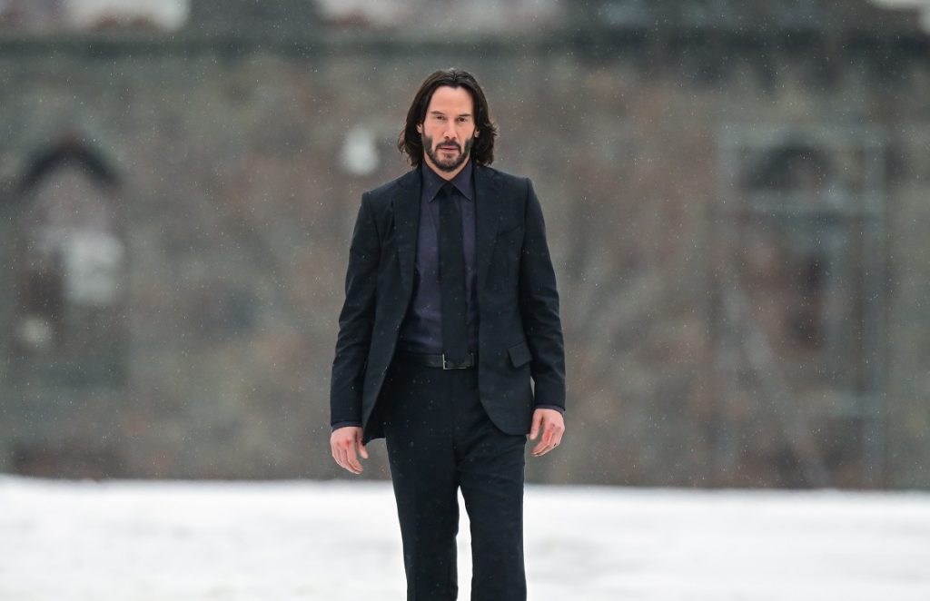 Keanu Reeves posant en portant un costume entièrement noir.