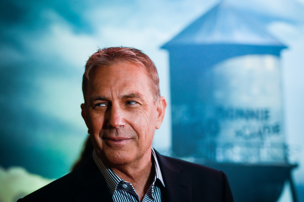 Kevin Costner sourit sur le tapis rouge avec un château d'eau en arrière-plan