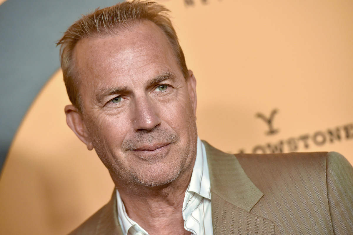 Kevin Costner porte un costume marron et sourit