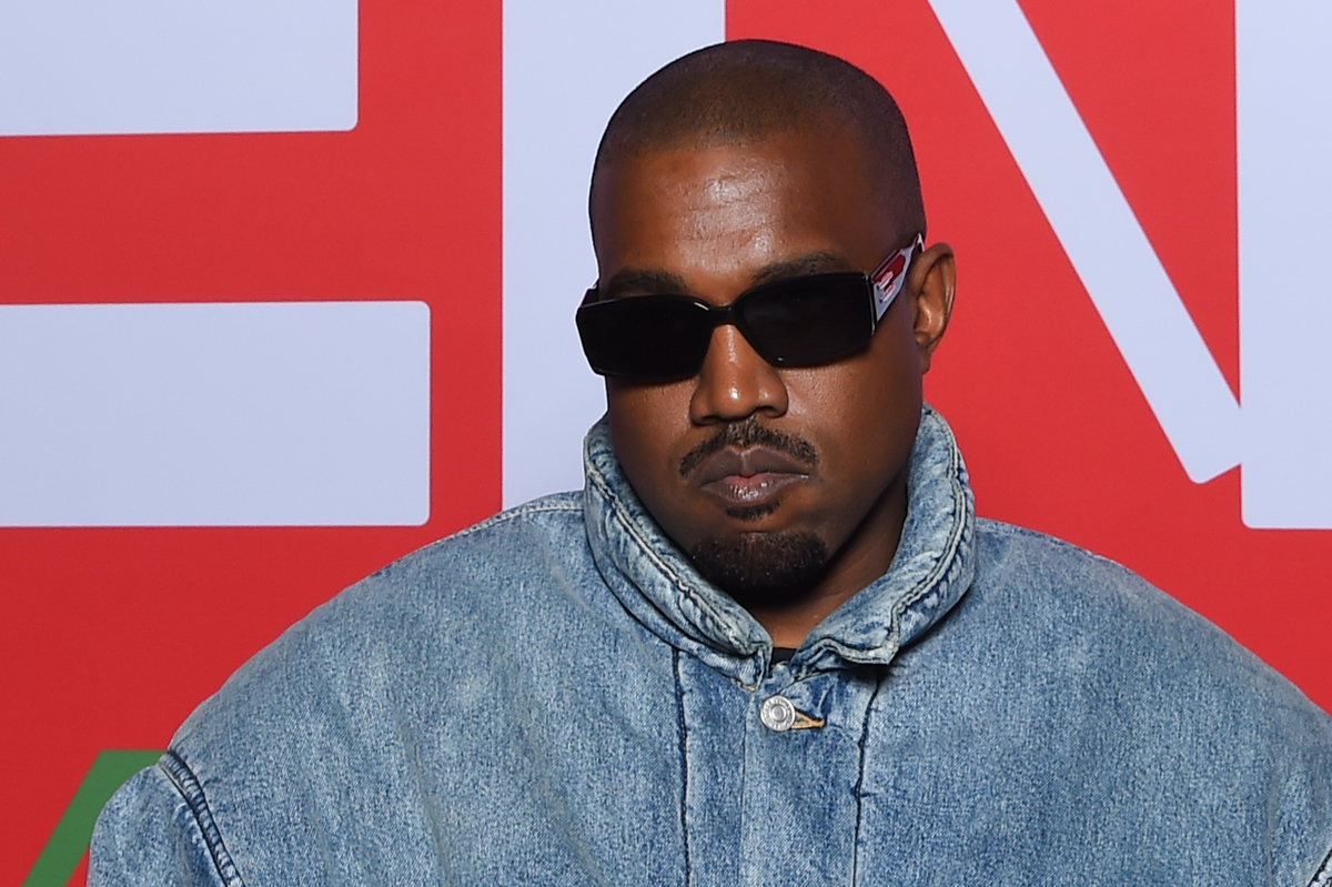 Kanye West dans une veste en jean et des lunettes de soleil noires pose avec un visage sévère.