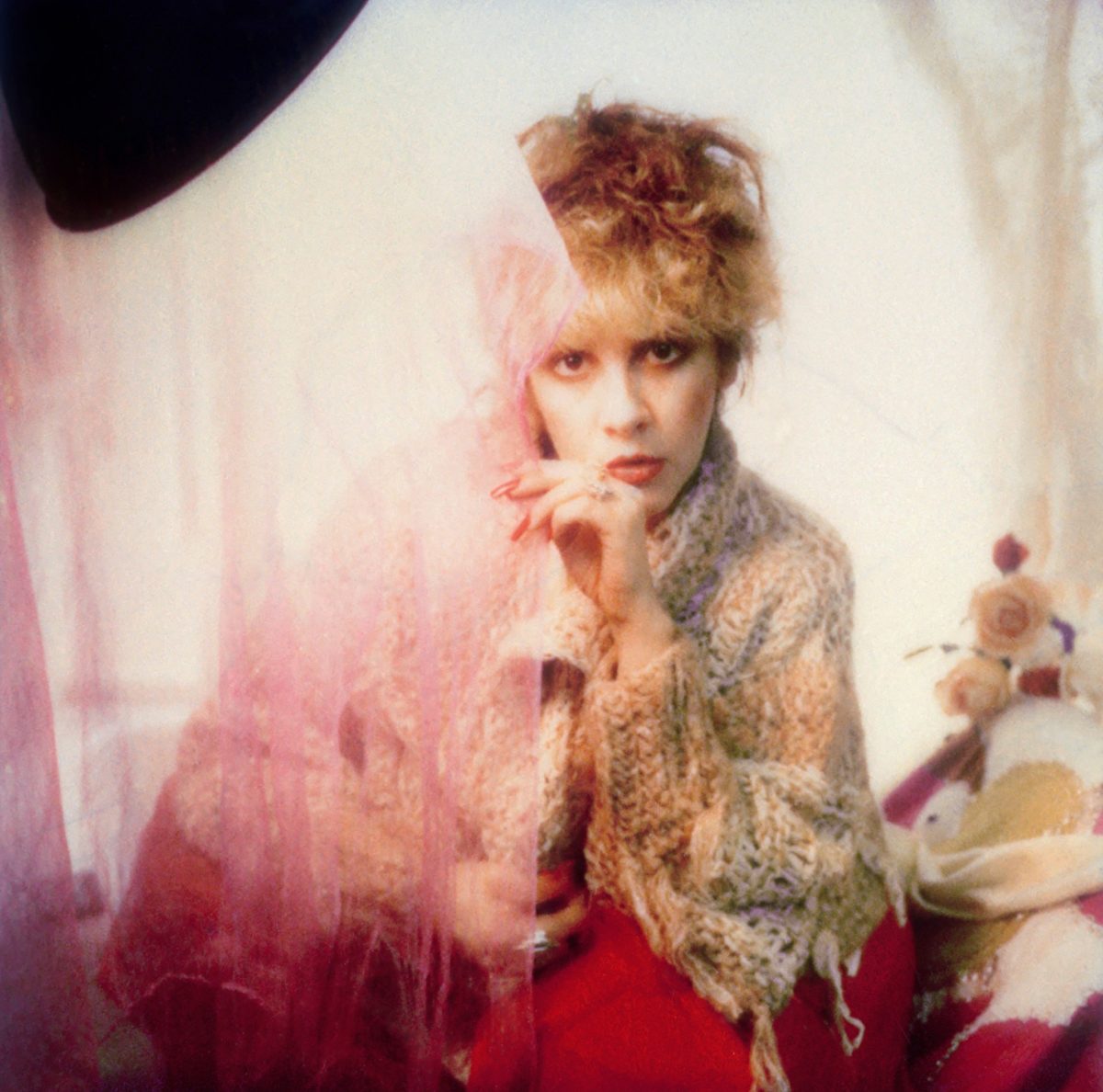 Stevie Nicks porte un pull en laine et jette un coup d'œil autour d'un rideau vaporeux.