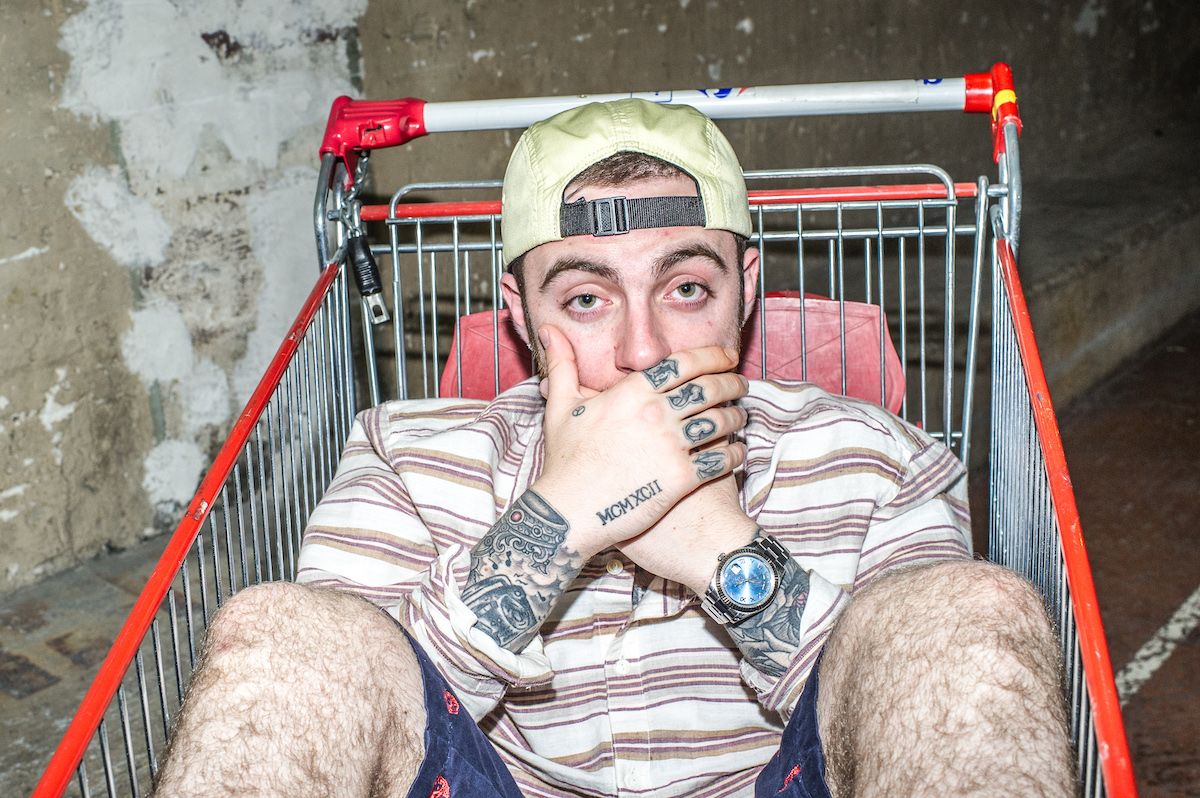 Mac Miller pose dans un caddie avec ses mains couvrant sa bouche.