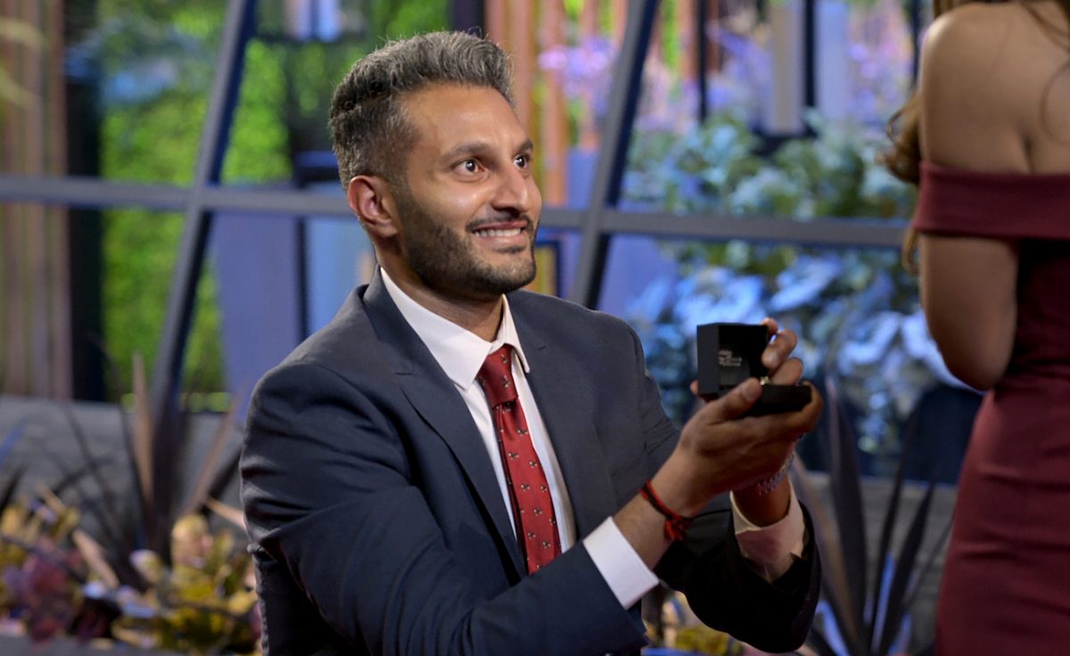 Shake Chatterjee présentant une boîte à bagues à quelqu'un lors d'une scène de 