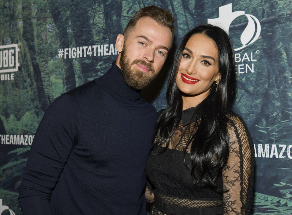 Artem Chigvintsev vêtu d'un col roulé noir pose avec la fiancée Nikki Bella, qui porte également une tenue noire. 