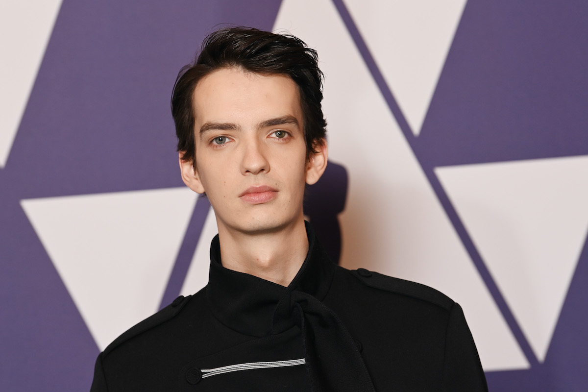 Kodi Smit-McPhee pose en noir devant un logo violet des Oscars