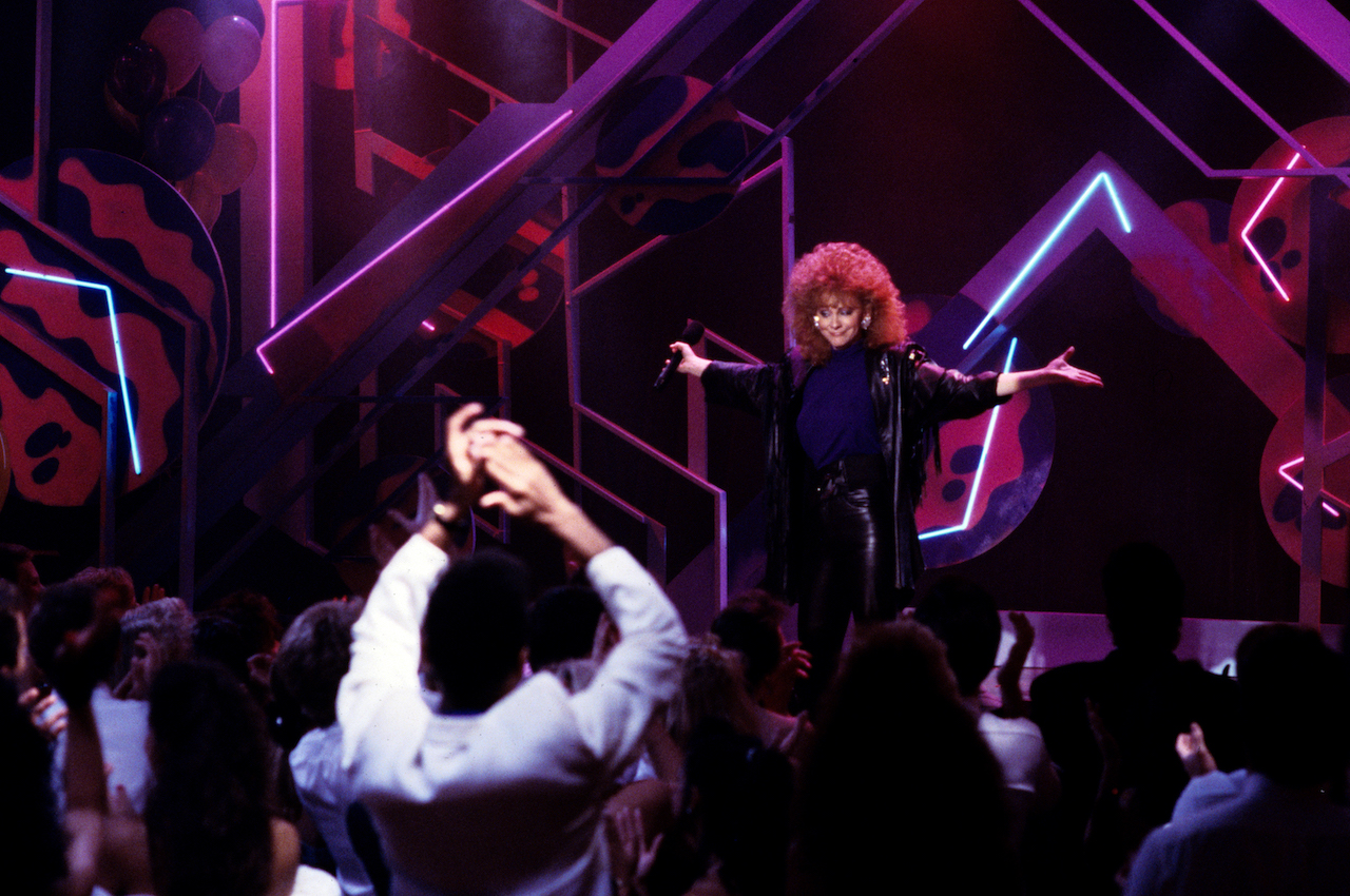 Reba McEntire se produit sur scène, tenant ses mains sur le côté c. 1989