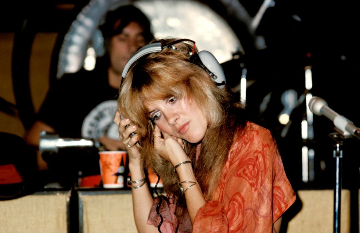 Stevie Nicks porte des écouteurs gris et une chemise orange.