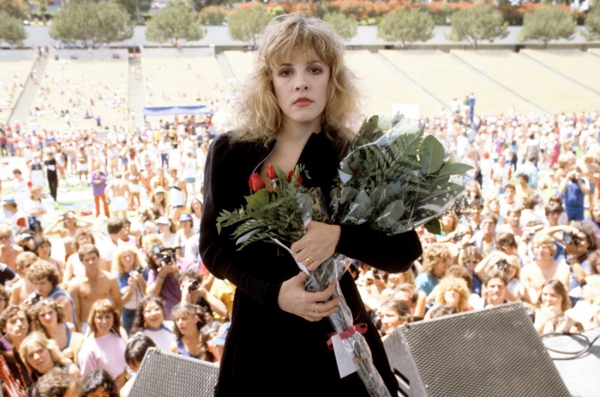 Stevie Nicks se tient sur scène et tient un bouquet de fleurs.