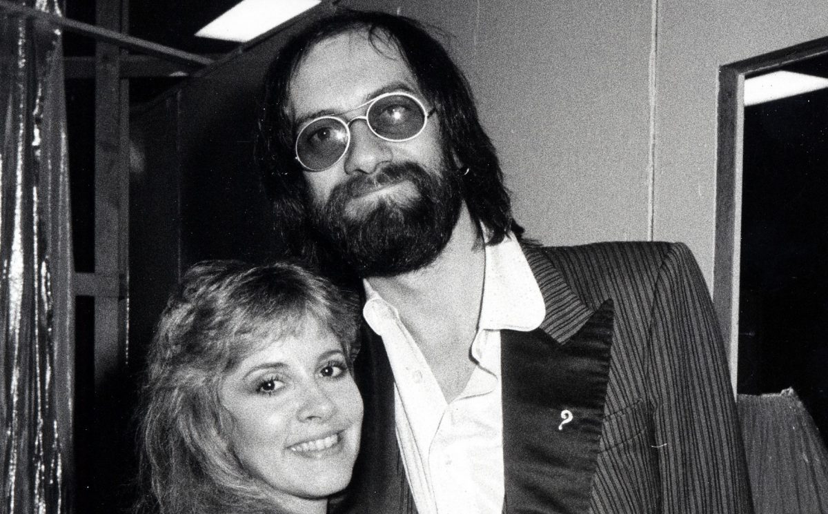 Une photo en noir et blanc de Stevie Nicks et Mick Fleetwood souriant ensemble.  Il porte des lunettes de soleil.