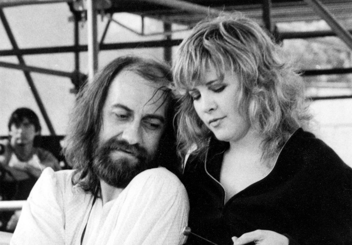 Une photo en noir et blanc de Mick Fleetwood assis et de Stevie Nicks debout juste derrière lui.