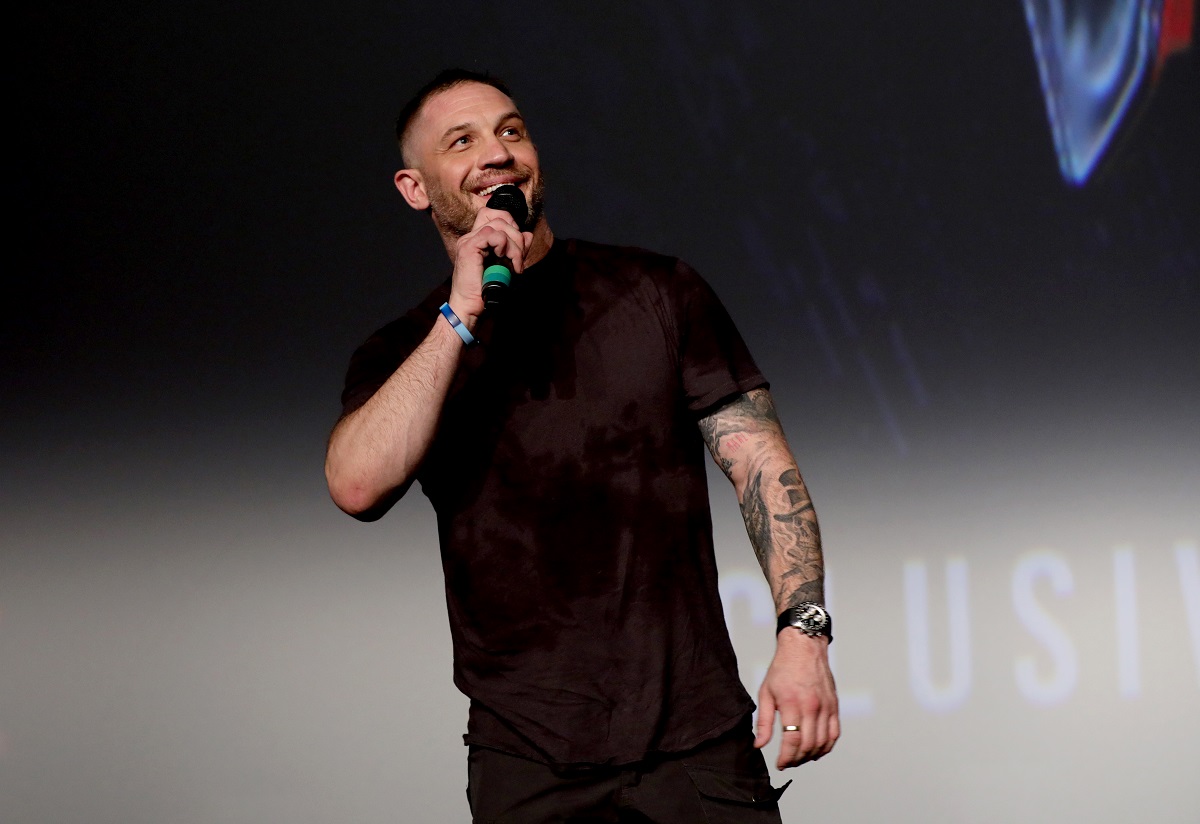 Tom Hardy souriant tout en tenant un microphone.