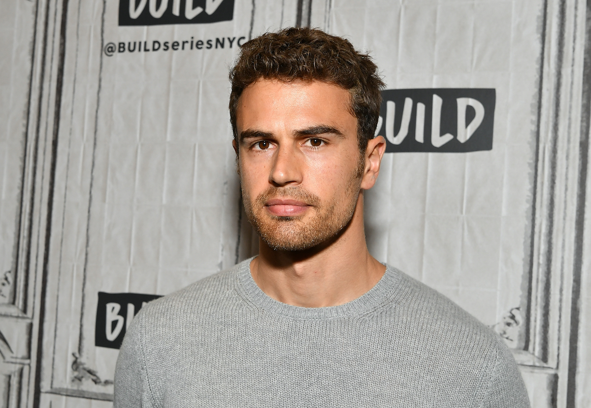 Theo James, ancien de Downton Abbey, porte une chemise grise et regarde la caméra