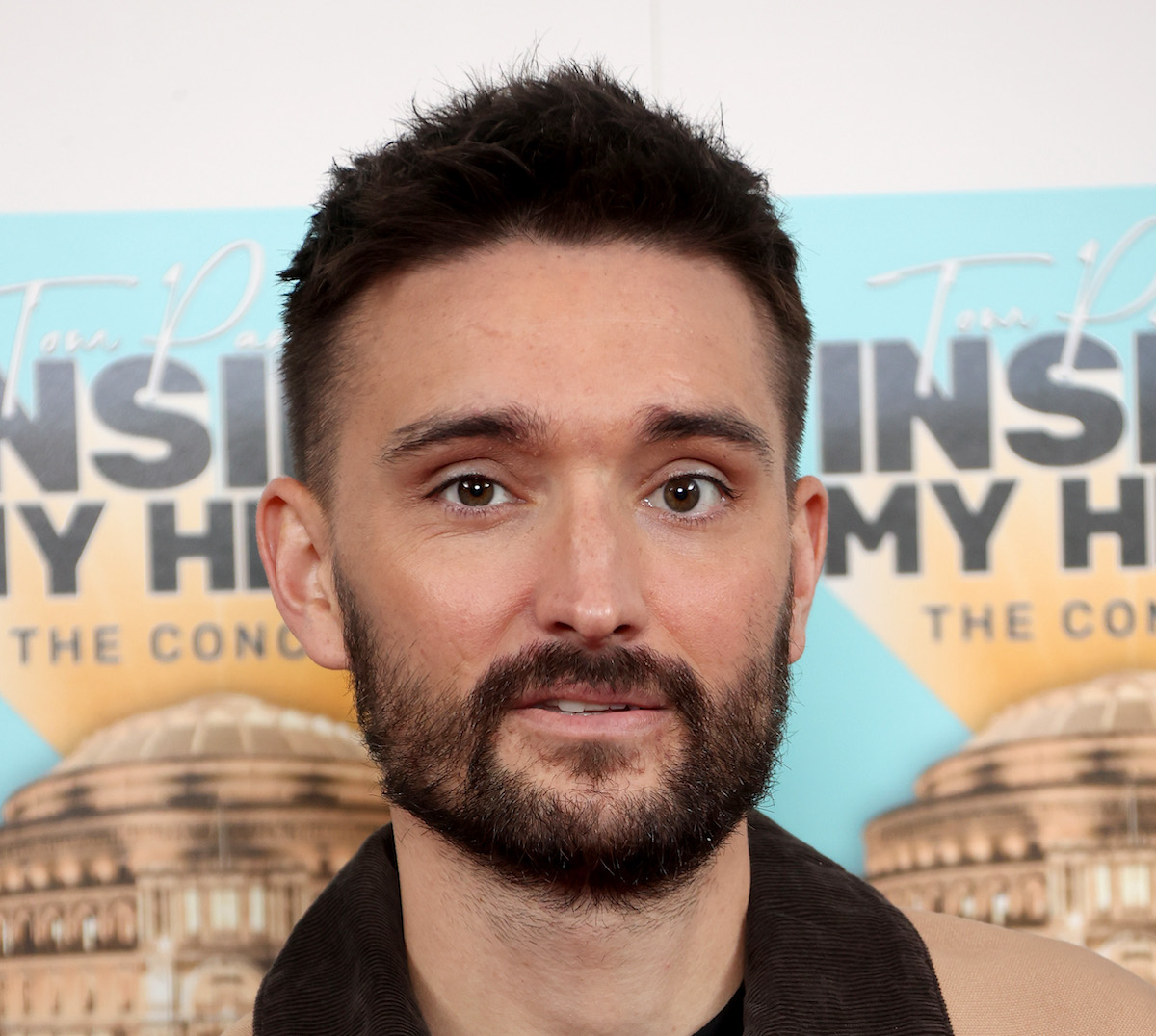 Tom Parker de The Wanted porte une veste marron alors qu'il pose pour les caméras