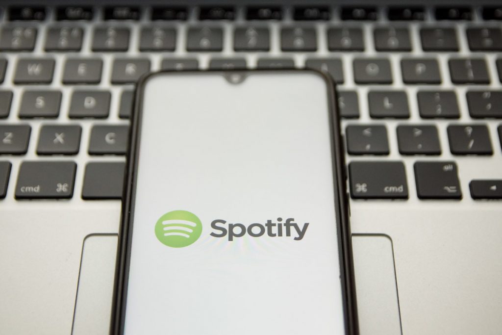Un logo Spotify s'affiche sur l'écran d'un smartphone avec un mot-clé d'ordinateur en arrière-plan