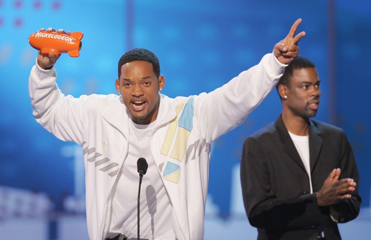 Will Smith aux Kids Choice Awards acceptant un prix avec Chris Rock en arrière-plan.  Will Smith est debout avec enthousiasme sur le podium tenant son prix.