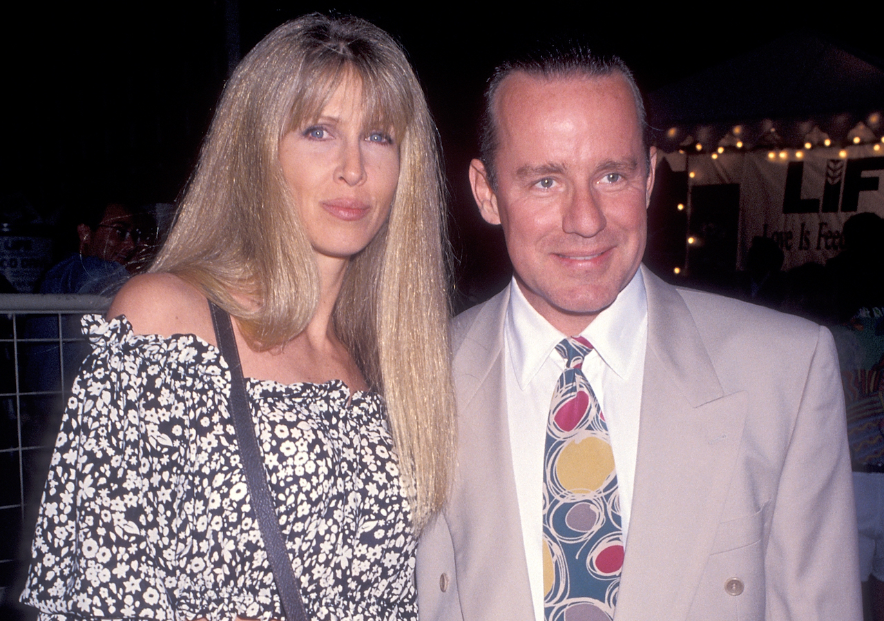 Brynn Hartman dans un haut noir et blanc, posant avec Phil Hartman dans un costume beige et une cravate à motifs.
