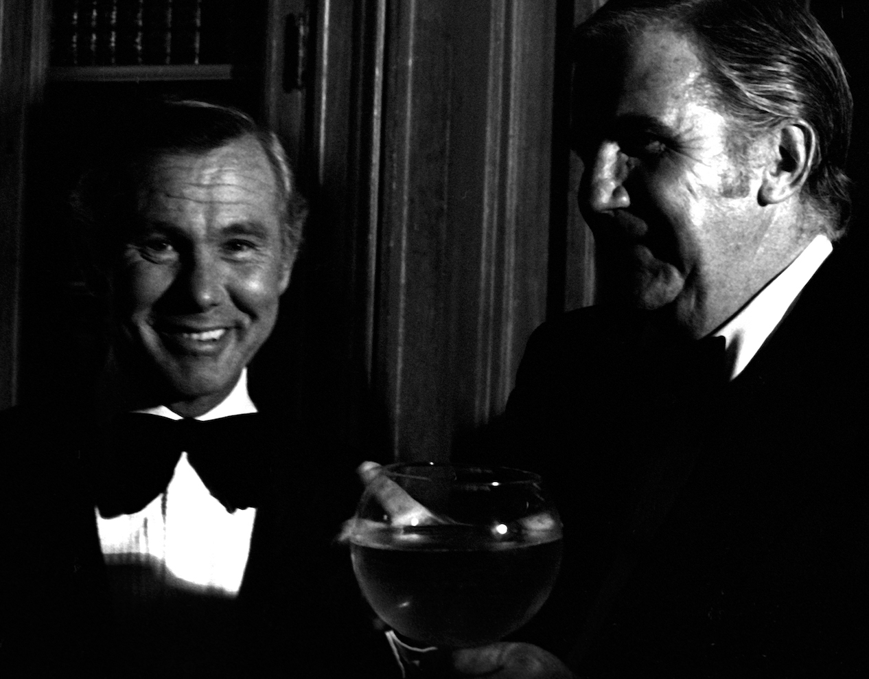 Photo en noir et blanc de Johnny Carson et Ed McMahon en smoking.  McMahon tient un grand verre de vin.