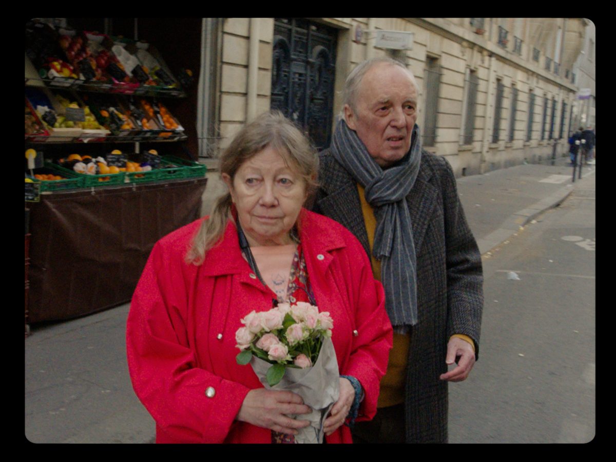 'Vortex' Françoise Lebrun comme Elle et Dario Argento comme Lui avec Lebrun tenant des fleurs dans une veste rouge marchant dans la rue devant un magasin